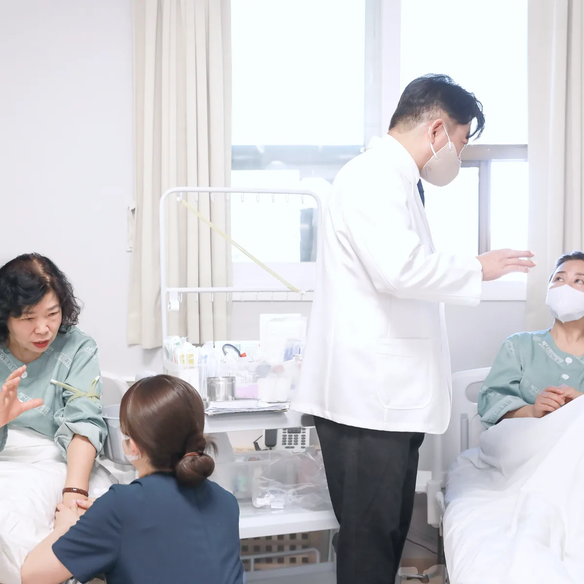 병실 회진에서 원장이 항암 치료 중인 환자의 이야기를 듣고 간호사가 곁에서 상태를 살피는 모습