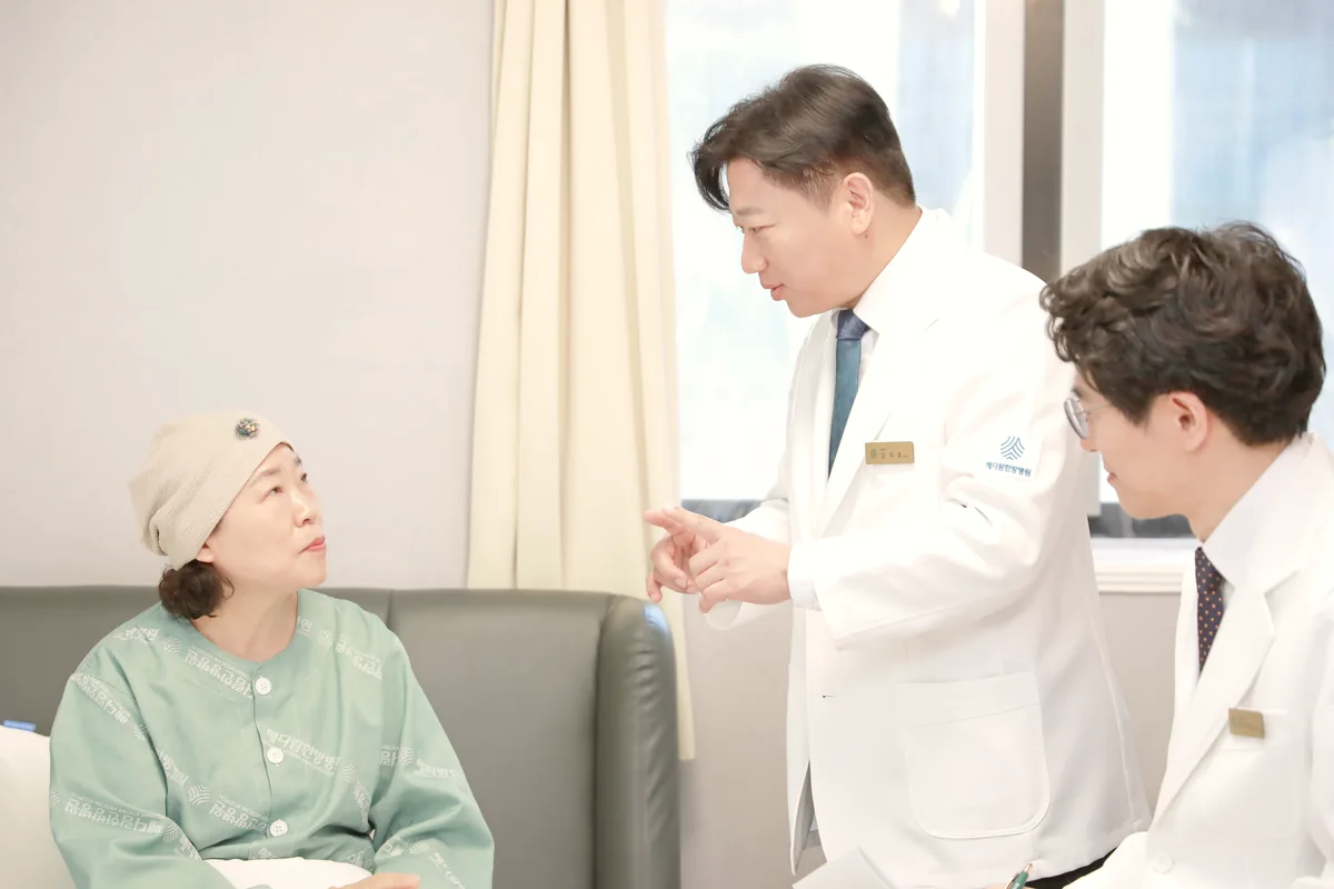 두건을 쓴 환자에게 두 원장이 병실 소파 앞에서 치료 중 몸 상태 확인 방법을 설명하는 모습