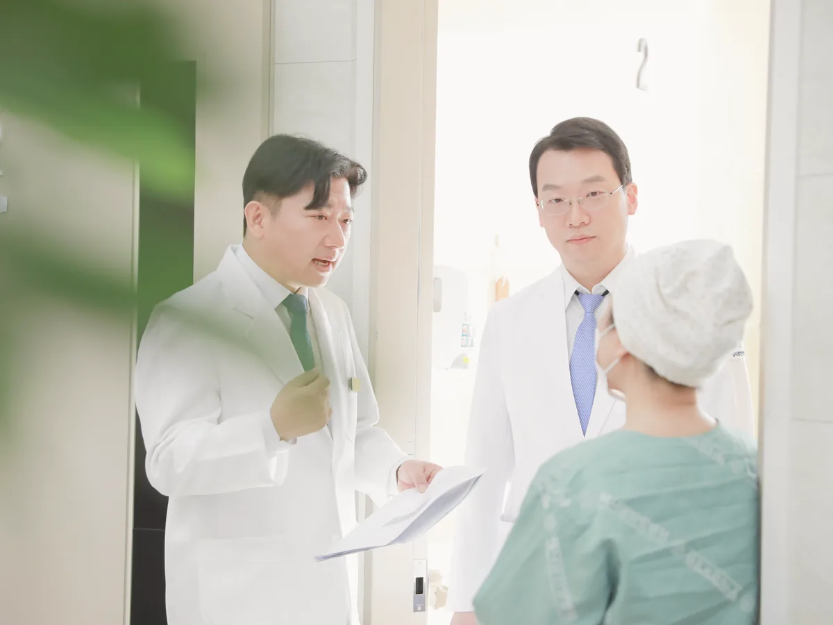 두 원장이 병실 문 앞에서 두건을 쓴 환자에게 퇴원 후 먹을 약과 줄여 가는 일정을 종이로 짚어 설명하는 모습