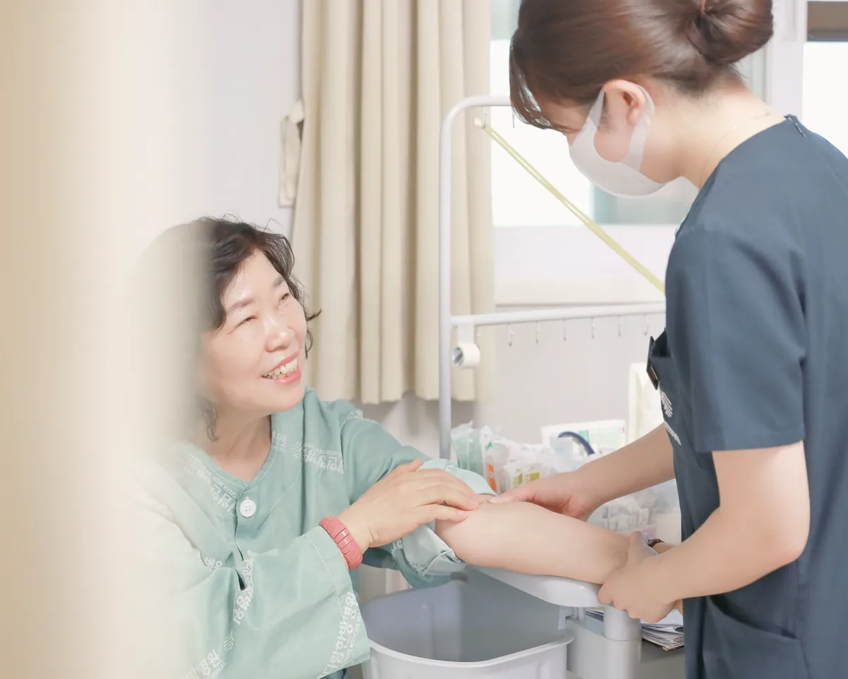 간호사가 시스플라틴 투여 전 수액을 연결할 환자의 팔 상태를 살피고 웃으며 이야기하는 모습