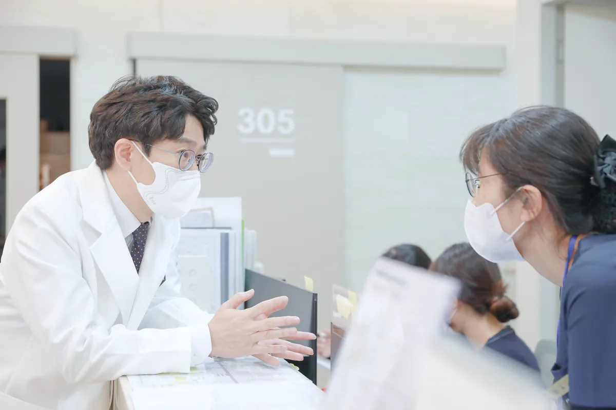 의료진이 보호자에게 대장암 수술 후 추적검사 일정과 전이 검사 결과를 설명하는 장면