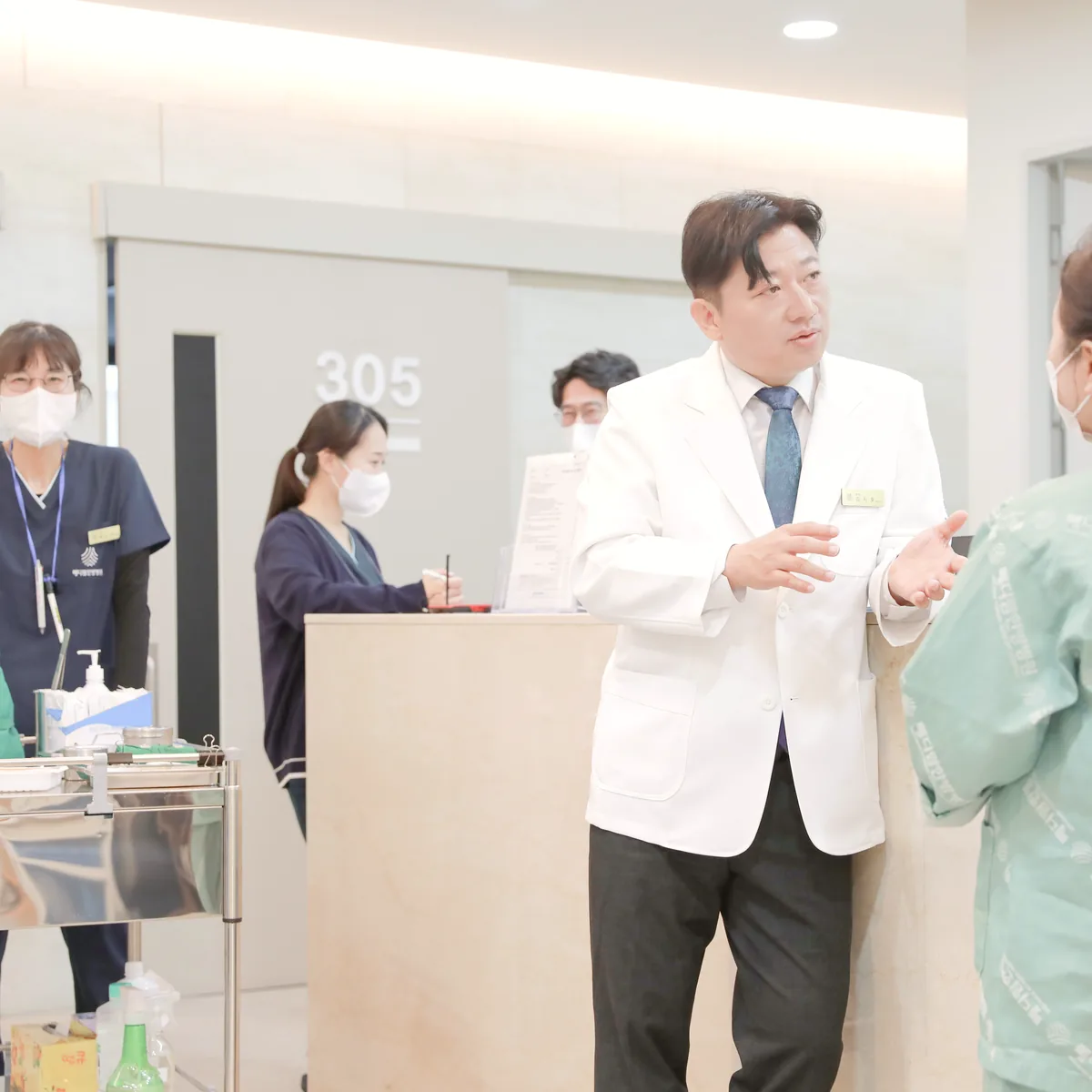 간호사실 앞에서 원장이 환자복을 입은 환자에게 다음 항암 주기의 몸 상태 확인 방법을 설명하는 모습