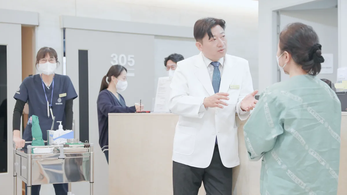 원장이 간호사실 앞에서 입원 환자와 지금 먹고 있는 약에 대해 이야기를 나누는 모습