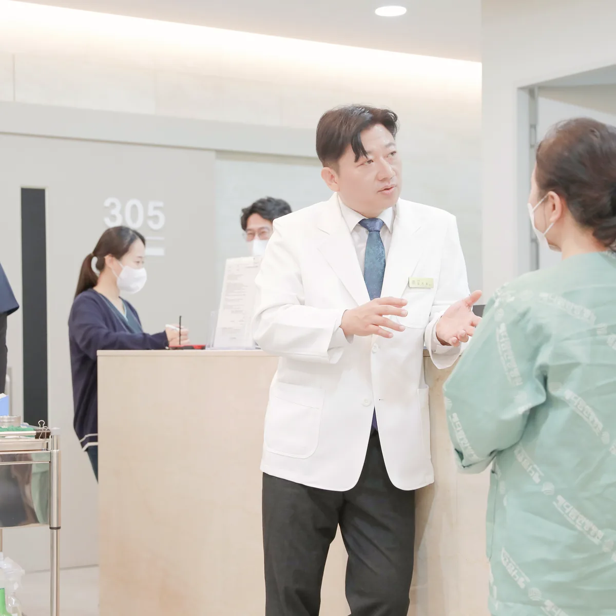 간호사실 앞에서 원장이 입원 환자와 마주 서서 식사량과 몸 상태를 묻는 모습