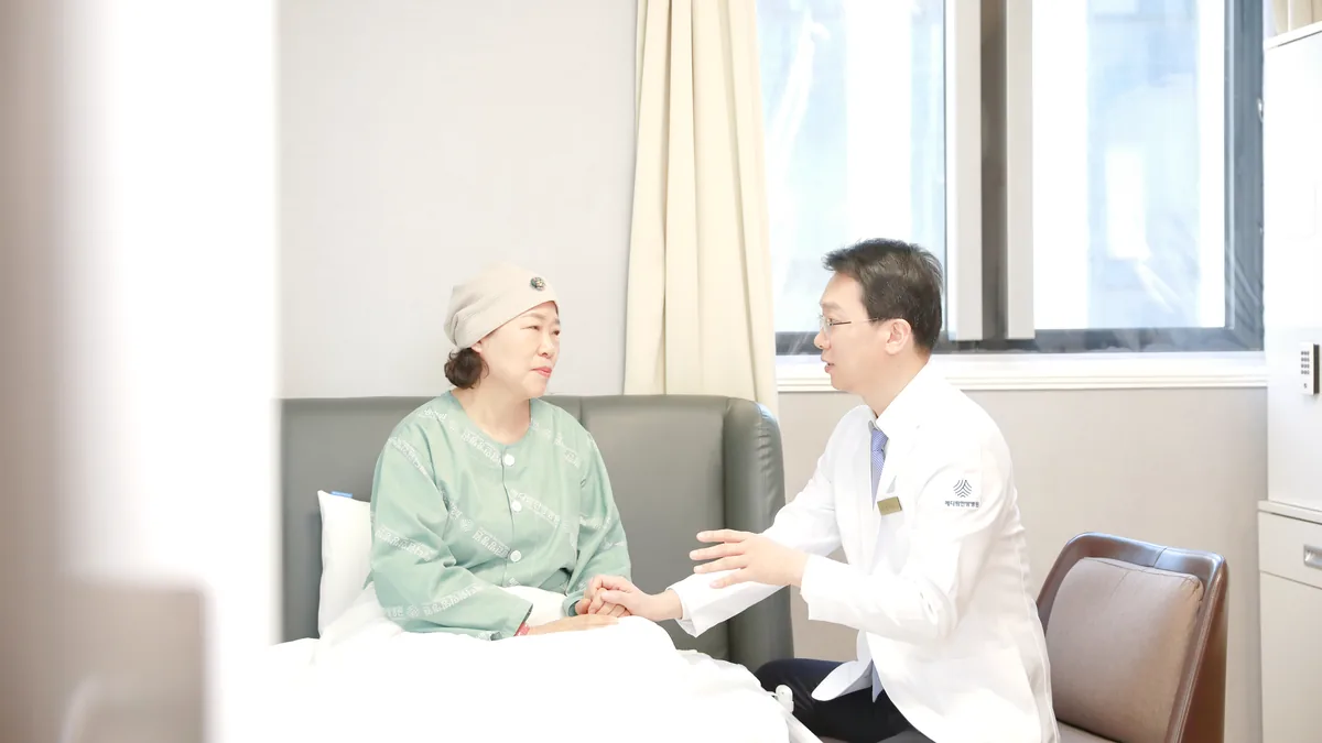 원장이 병실 침대에 앉은 환자의 손을 잡고 항암 기간 몸 상태를 묻고 있는 모습