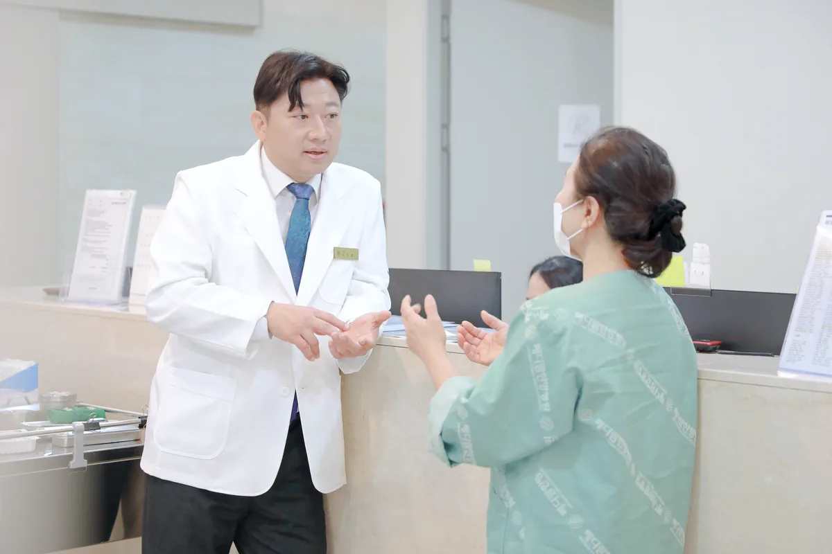 간호사실 앞에서 원장이 회복 중인 환자에게 식사 뒤 변 상태와 몸무게 변화를 묻고 설명하는 모습