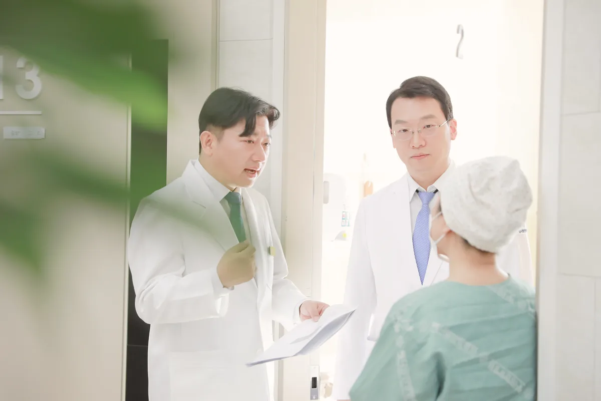 병실 앞에서 두 원장이 수술 뒤 회복 중인 환자와 서류를 보며 다음 관리 계획을 이야기하는 모습