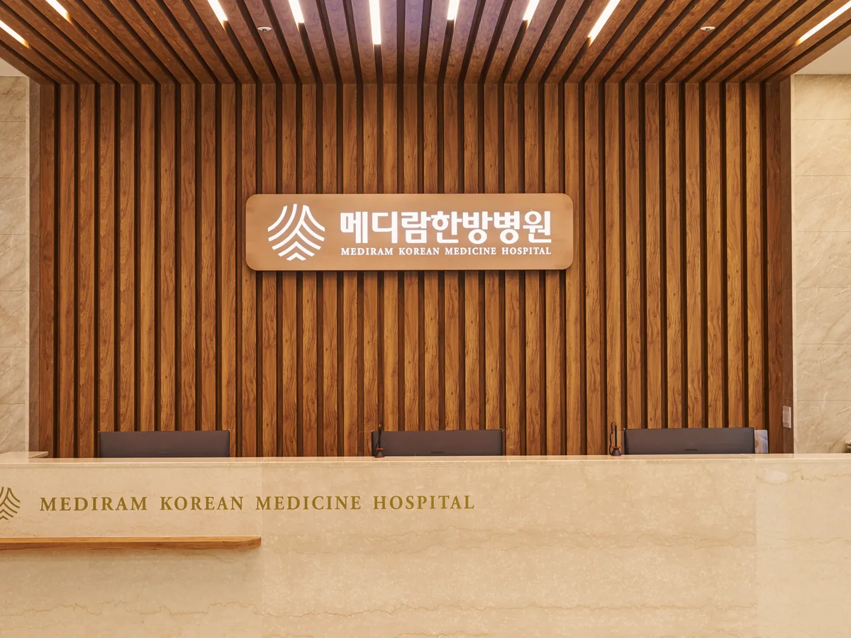나무 루버 벽에 병원 이름이 걸린 메디람한방병원 1층 안내 데스크