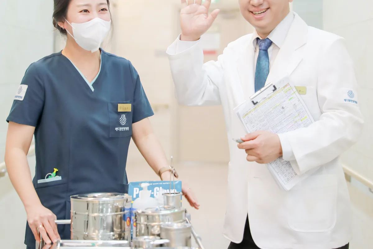 병동 복도에서 원장이 투약 카트를 미는 간호사와 인사하며 회진을 시작하는 모습