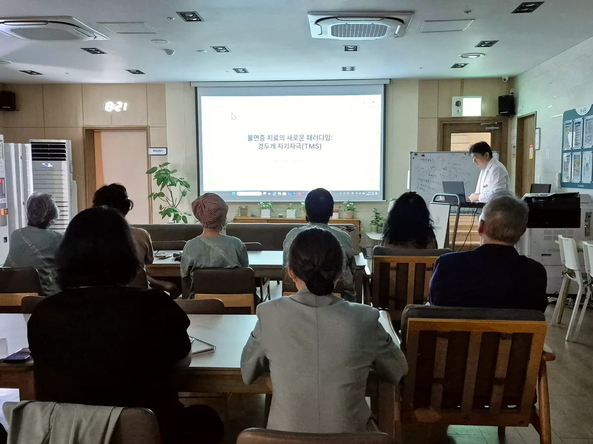 원내 강연장에서 김지호 병원장이 불면증과 경두개 자기자극 강의를 시작하고 환자와 보호자들이 화면을 보며 듣는 모습